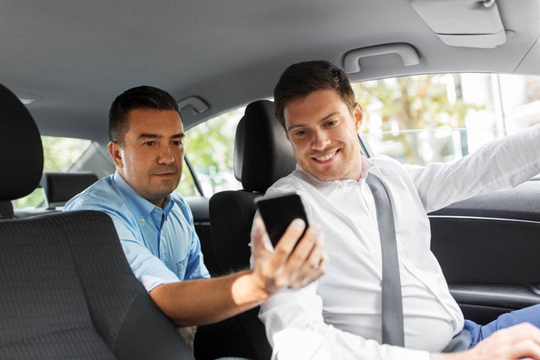 male passenger showing smartphone to car driver - 写真・画像