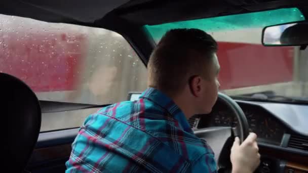 Nuori mies ajaa autoa. Sateinen sää. Näkymä takapenkiltä tulevasta miehestä - Materiaali, video