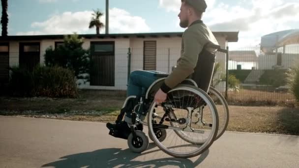 Młody mężczyzna z sparaliżowanymi nogami na wózku spaceruje samotnie na ulicach miasta - Materiał filmowy, wideo
