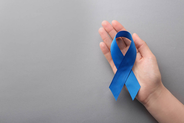 Woman holding blue awareness ribbon on grey background, top view with space for text. Symbol of social and medical issues - Фото, изображение