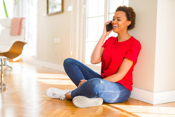 Kaunis nuori afrikkalainen amerikkalainen nainen istuu lattialla ottaa keskustelun puhelimessa hymyillen
 - Valokuva, kuva