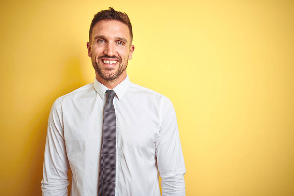 Jonge knappe zakenman draagt elegant wit shirt over gele geïsoleerde achtergrond met een vrolijke en coole glimlach op het gezicht. Geluksvogel. - Foto, afbeelding
