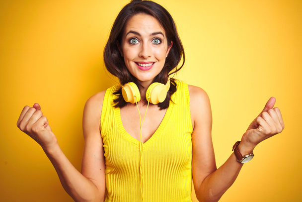 Young beautiful woman wearing headphones over yellow isolated background celebrating surprised and amazed for success with arms raised and open eyes. Winner concept. - Photo, Image