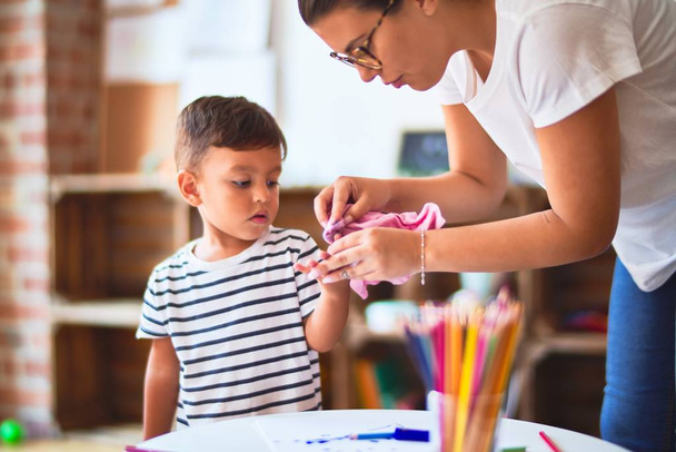 Belle enseignante et enfant en bas âge dessin de garçon à l'aide de crayons de couleur à la maternelle
 - Photo, image