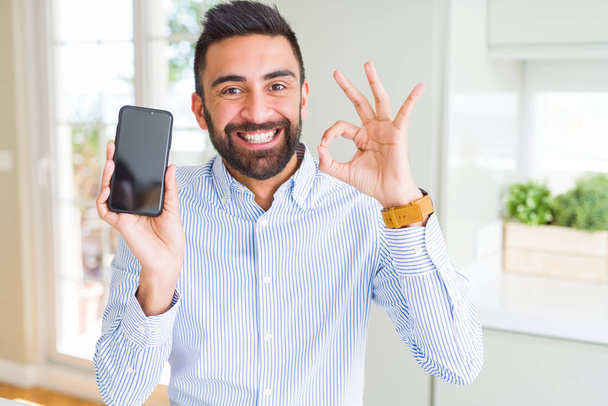 Красивий іспаномовний бізнесмен, що показує екран смартфона, робить знак з пальцями, відмінний символ
 - Фото, зображення