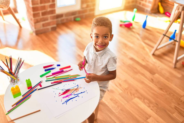 Прекрасний афроамериканець малює з паперу і маркер, які посміхаються в дитячому садку. - Фото, зображення