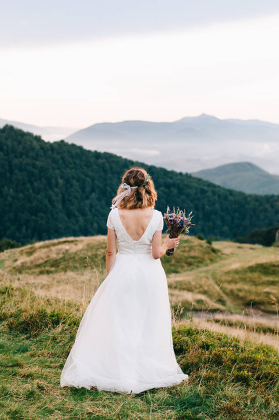 Panna Młoda trzyma ślub bukiet kwiatów lawendy. Elegancka Newlywed Photosession w górach. - Zdjęcie, obraz