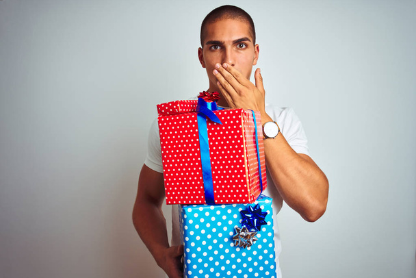 Young handsome man holding birthday gifts over white isolated background cover mouth with hand shocked with shame for mistake, expression of fear, scared in silence, secret concept - Fotoğraf, Görsel