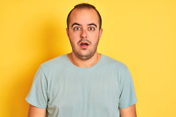 Young man wearing green casual t-shirt standing over isolated yellow background afraid and shocked with surprise expression, fear and excited face. - Photo, Image