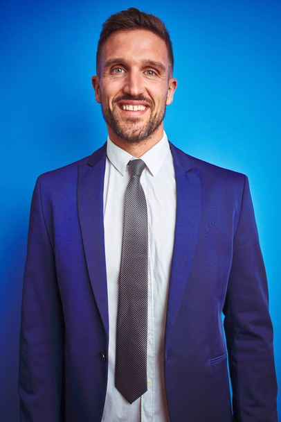 Vertical angle picture of young handsome business man over blue isolated background with a happy and cool smile on face. Lucky person. - Photo, image