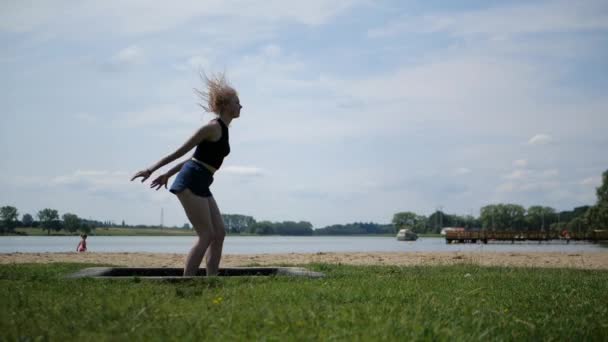 Enerjik neşeli kız sarışın güzel doğada bir trambolin atlar - Video, Çekim