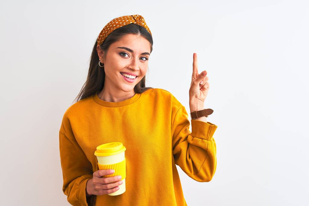 Nuori kaunis nainen juo lasi ottaa pois kahvia yli eristetty valkoinen tausta erittäin onnellinen osoittaa käsin ja sormella sivulle
 - Valokuva, kuva