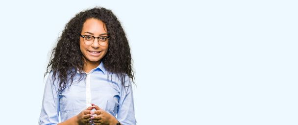 Young beautiful business girl with curly hair wearing glasses Hands together and fingers crossed smiling relaxed and cheerful. Success and optimistic - Photo, Image