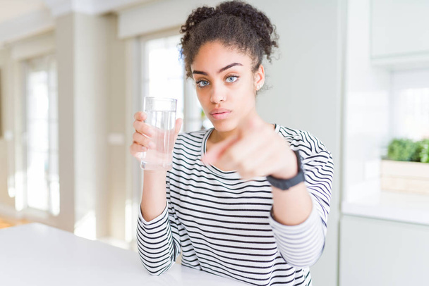 Mladá africká americká dívka pije čerstvou sklenici vody ukazující prstem na fotoaparát a na vás, znak ruky, pozitivní a sebevědomé gesto zepředu - Fotografie, Obrázek