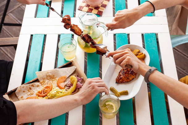 Les jeunes hommes et les jeunes femmes mangent sur la terrasse d'été : poitrine de poulet barbecue grillée aux pommes de terre cuites au four et poulet grillé aux pommes de terre croustillantes
 - Photo, image
