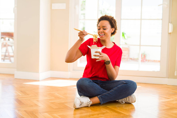 床に座って choopsticks を使用して麺を食べて美しい若いアフリカ系アメリカ人女性 - 写真・画像