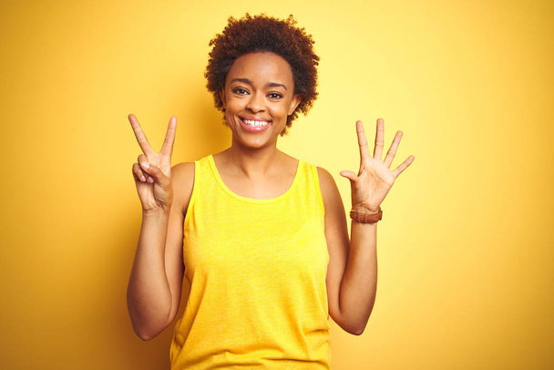 Beauitul afrikai-amerikai nő visel nyári póló alatt elszigetelt sárga háttér mutatja, és rámutatva ujjaival száma hetes, miközben mosolyogva magabiztos és boldog. - Fotó, kép