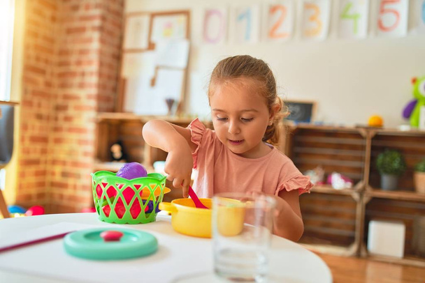 Beautiful blond toddler girl playing  meals using plastic food at kindergarten - 写真・画像