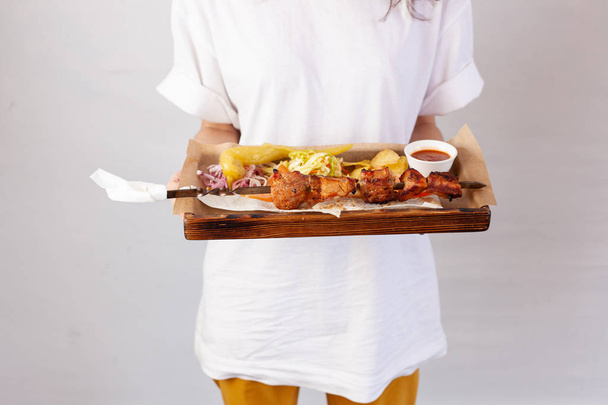 Официантка держит поднос с праздничными закусками: курица-гриль, картофельные чипсы, капустный салат и овощи
 - Фото, изображение