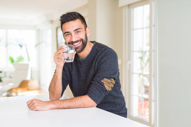 Красивий іспаномовний чоловік п'є свіжу склянку води з щасливим обличчям, що стоїть і посміхається з впевненою посмішкою, показуючи зуби
 - Фото, зображення