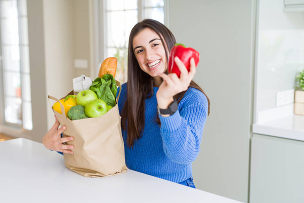 Young beautiful woman smiling holding a paper bag full of grocer - Photo, Image