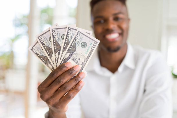 Hombre afroamericano sosteniendo billetes de cincuenta dólares con una cara feliz de pie y sonriendo con una sonrisa confiada mostrando los dientes
 - Foto, Imagen