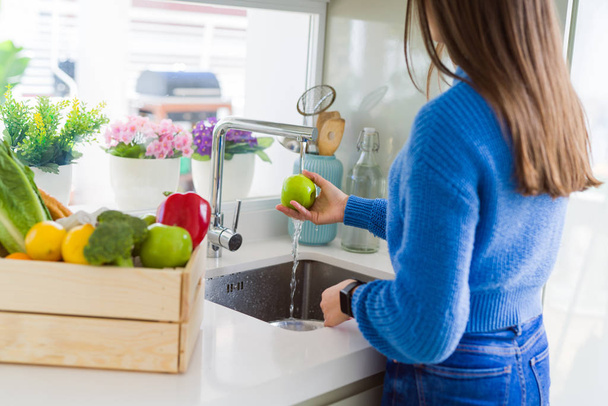 Молода жінка миє овочі та фрукти, використовуючи воду з раковини
 - Фото, зображення
