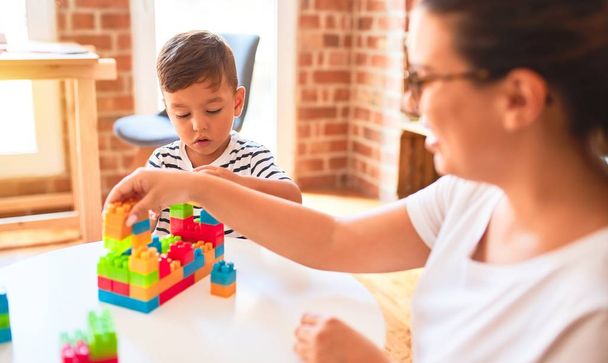 Beautiful teacher and toddler boy playing with construction blocks bulding tower at kindergarten - 写真・画像