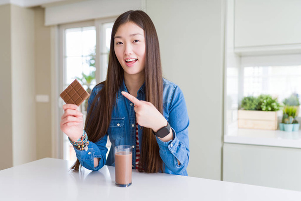 Gyönyörű ázsiai nő iszik csokis turmixot és tartja csokoládé bár nagyon boldog mutató kézzel és ujjal - Fotó, kép