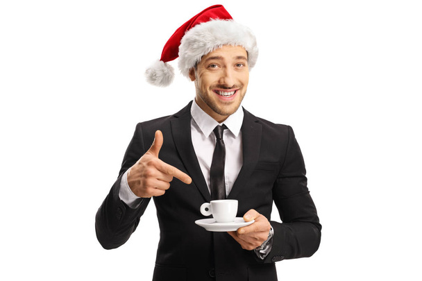 Man in a suit with a Santa hat holding a cup of coffee and point - Foto, afbeelding