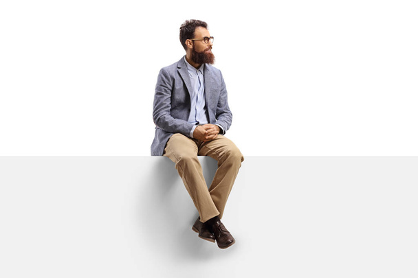 Bearded man sitting on a white banner and looking to the side - Foto, Imagem