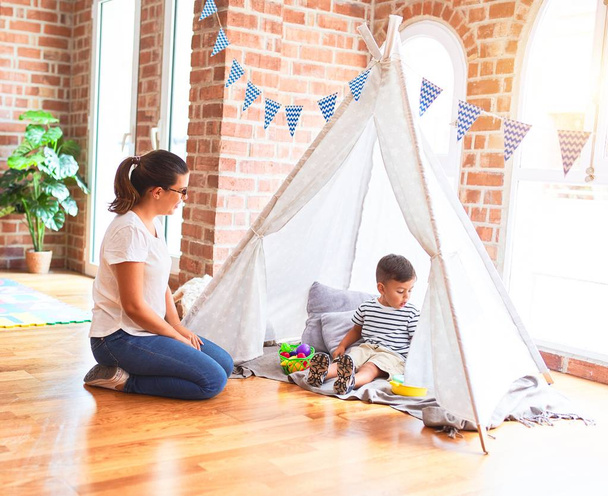 Beautiful teacher and toddler boy sitting on the floor playing inside  tipi at kindergarten - Foto, immagini