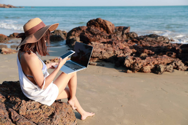 bella e carina donna d'affari che utilizza computer portatile e telefono cellulare con occhiali da sole e cappello sulla spiaggia durante le vacanze
 - Foto, immagini