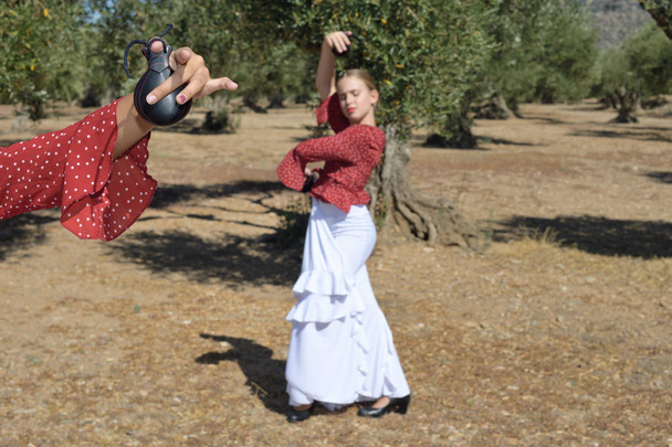 A mão de um bailarino mostra uma castanhola e ao fundo, embaçada, outra bailarina realiza um movimento flamenco
 - Foto, Imagem