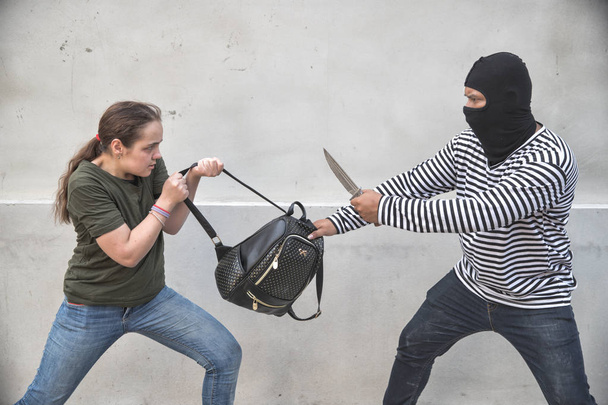 ナイフを手に路上で歩く女性からバッグを盗む泥棒(盗難コンセプト) - 写真・画像