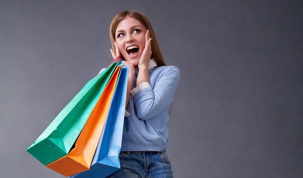 Sale, shopping, discount and Black Friday concept. Emotional girl with colored bags standing on a gray background. - Foto, Bild