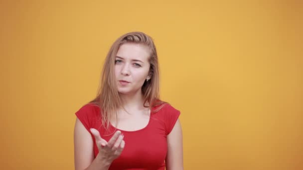 Mladá blondýnka v červeném tričku nad ojedinělým oranžovým pozadím vykazuje emoce - Záběry, video