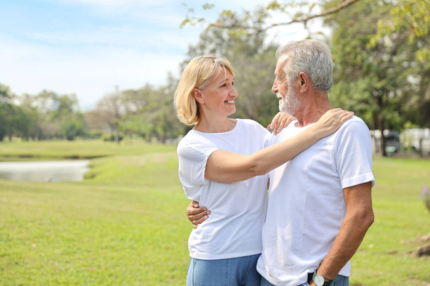 casal idoso sorridente com camisa branca e jean azul abraçando no parque no outono tempo com efeito de luz solar
 - Foto, Imagem