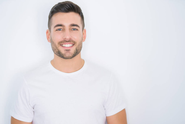 Jonge knappe man glimlachend gelukkig dragen casual wit t-shirt over witte geïsoleerde achtergrond - Foto, afbeelding