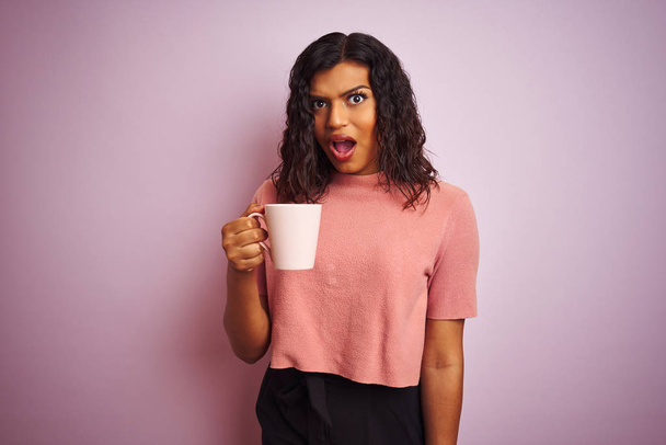 Транссексуальна транссексуальна жінка п'є чашку кави над ізольованим рожевим тлом, боїться шокувати з несподіваним обличчям, боїться і схвильований виразом страху
 - Фото, зображення