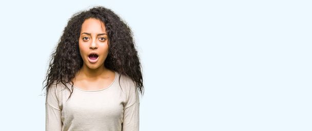 Young beautiful girl with curly hair wearing casual sweater afraid and shocked with surprise expression, fear and excited face. - Photo, Image