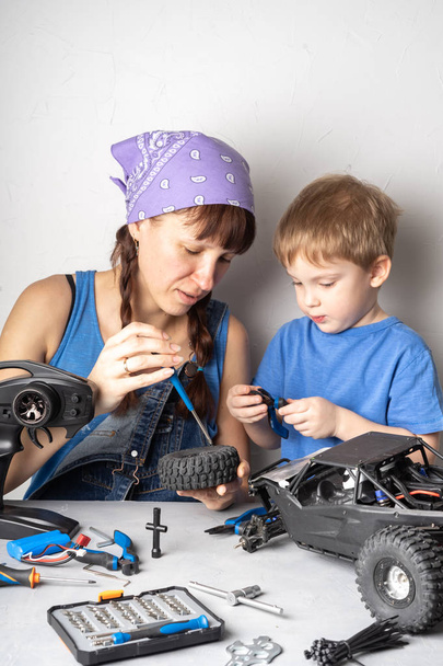 Women in the mens work: Mom helps her son with fixing a radio-controlled buggy model. - Foto, Imagem