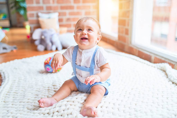 Gyönyörű kisbaba ül a takarón, mosolyog az óvodában. - Fotó, kép