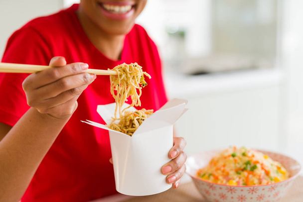Close up of young woman eating noodles from delivery box using choopsticks - Foto, Imagem