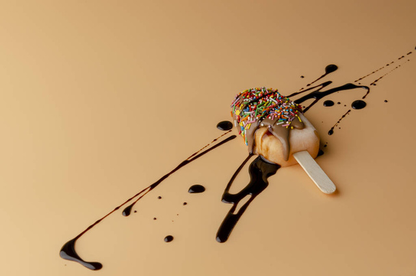 Oranje popsicle met chocolade glazuur met zwarte topping op pastel licht perzik achtergrond. - Foto, afbeelding