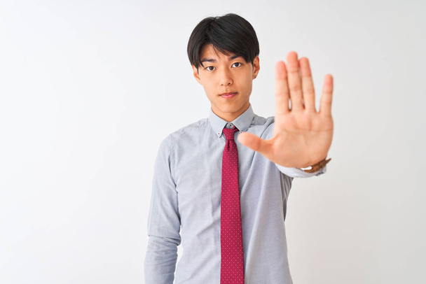 Homme d'affaires chinois portant une cravate élégante debout sur fond blanc isolé faire arrêter chanter avec la paume de la main. Expression d'avertissement avec geste négatif et sérieux sur le visage
. - Photo, image
