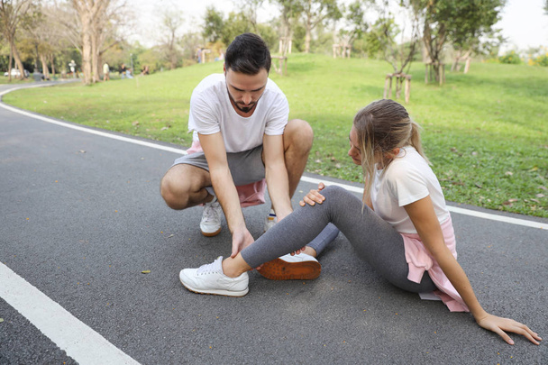 young girl in sport wear fall down because of the dizziness from too much exercise and young man is helping  - Photo, image