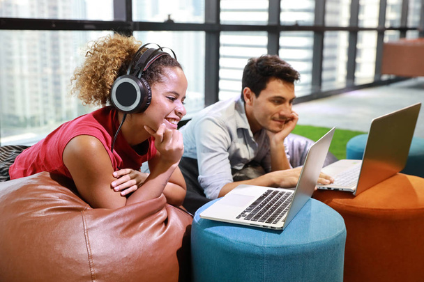 homme d'affaires caucasien et femme d'affaires en tenue décontractée intelligente écoutant la musique du casque et un autre travaillant sur ordinateur dans un bureau créatif avec un visage souriant et heureux
 - Photo, image