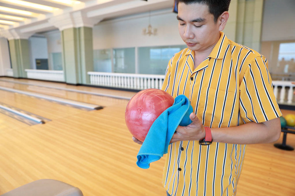 mladý asijský muž držící a čistícího bowlingovou kouli ve sportovním klubu - Fotografie, Obrázek
