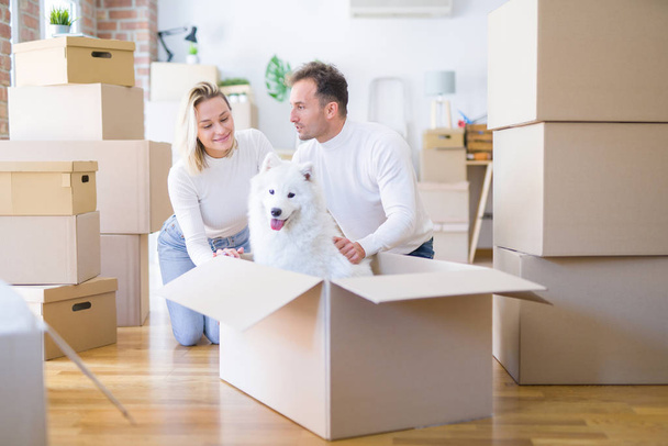Молодая красивая пара с собакой сидит на полу в новом доме вокруг картонных коробок
 - Фото, изображение